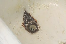 Deep eroded tub surface from dripping faucet, the drain must be removed for proper repair.