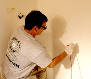 Tech using an airbrush for acrylic shower chip repair.